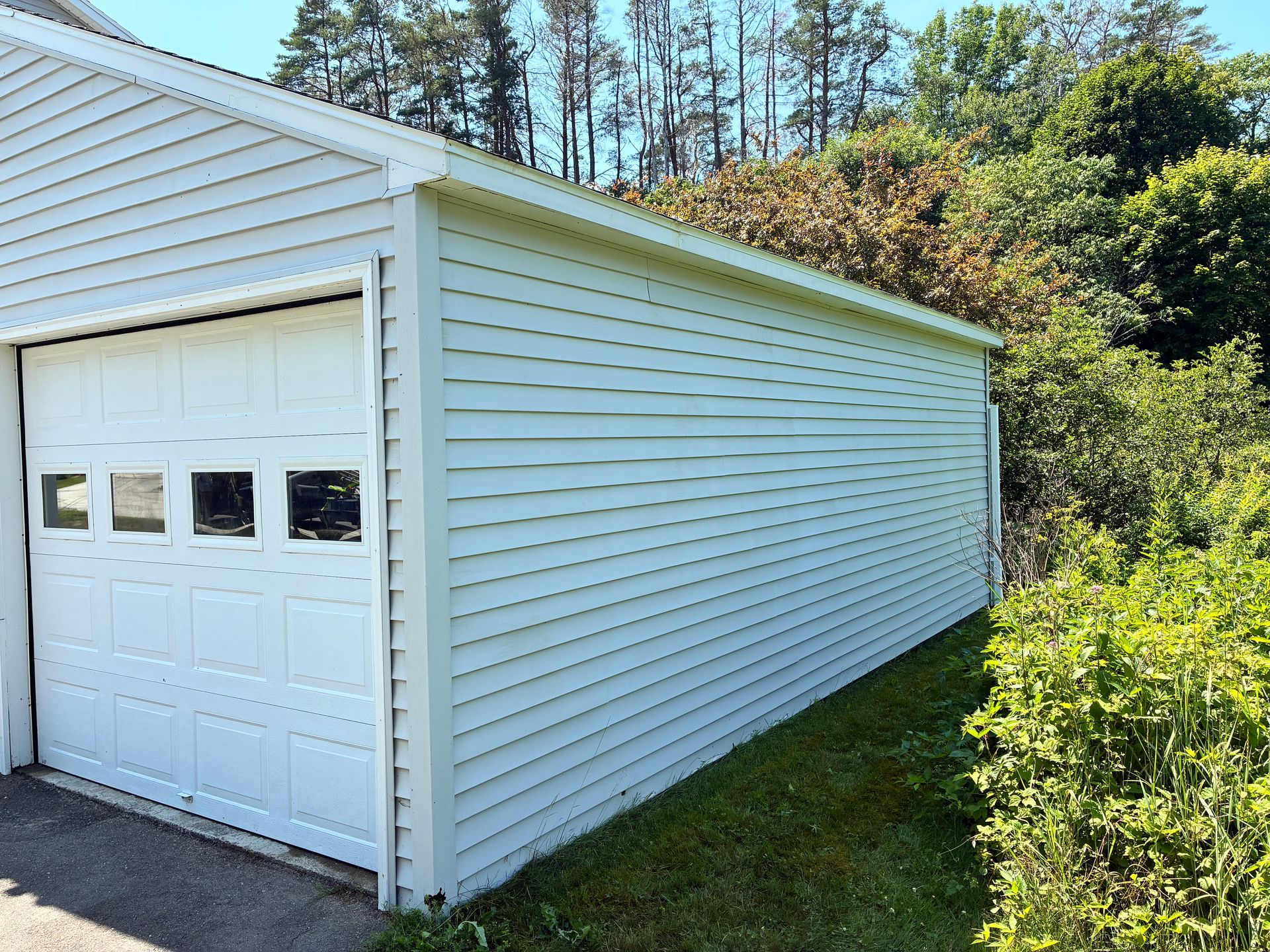 White detached garage with side view, white siding, and a grassy yard beside trees