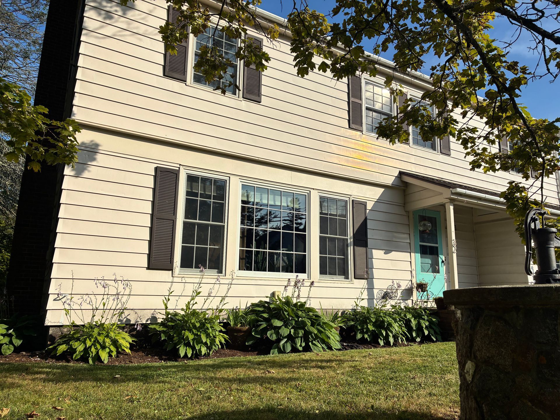 Two-story beige house with gray shutters, turquoise door, and front yard in sunlight