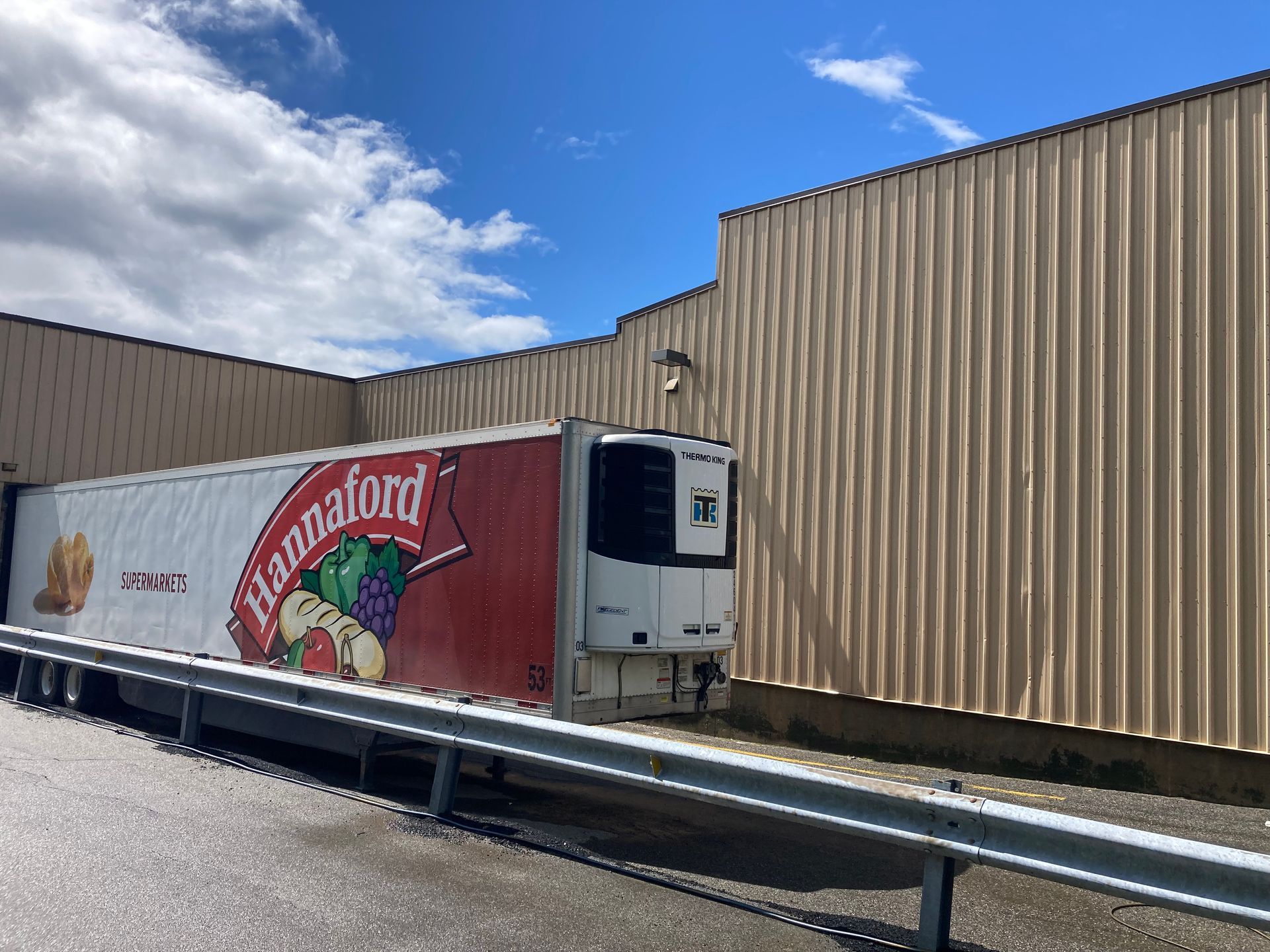 Pura Fruit truck parked beside a tan warehouse under a partly cloudy sky