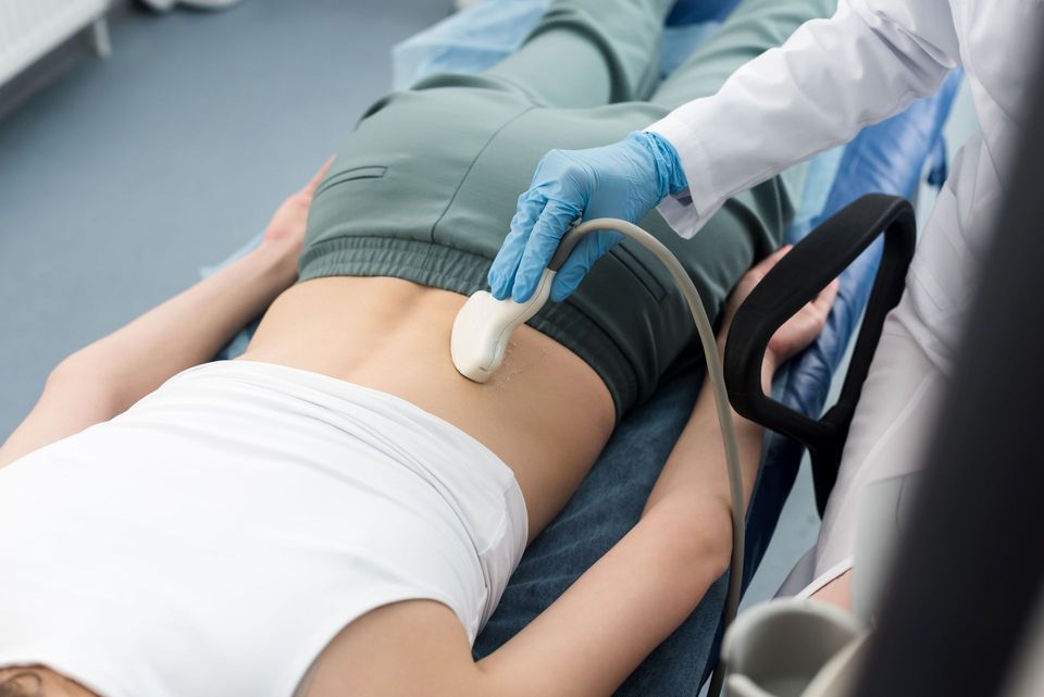 Un operatore sanitario utilizza una sonda a ultrasuoni sulla parte bassa della schiena di un paziente sdraiato su un lettino da visita.