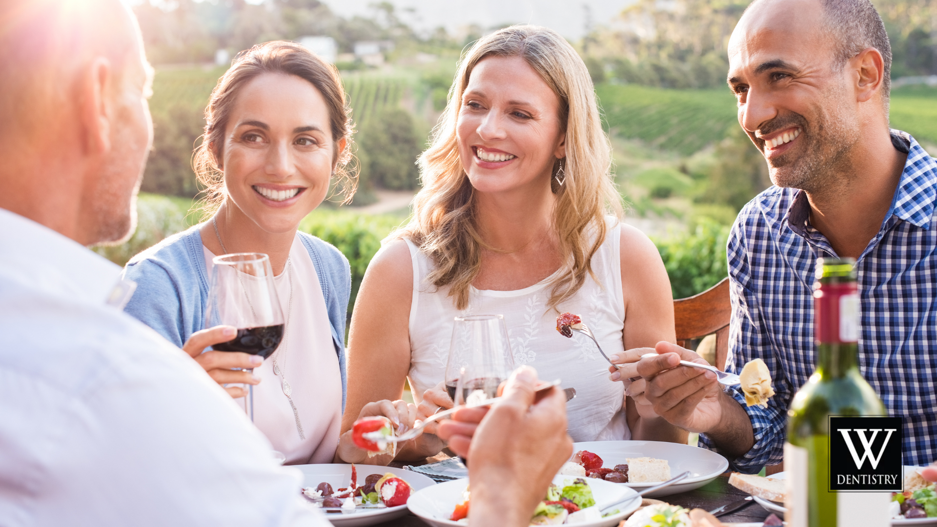 A group of people are sitting at a table eating food and drinking wine.