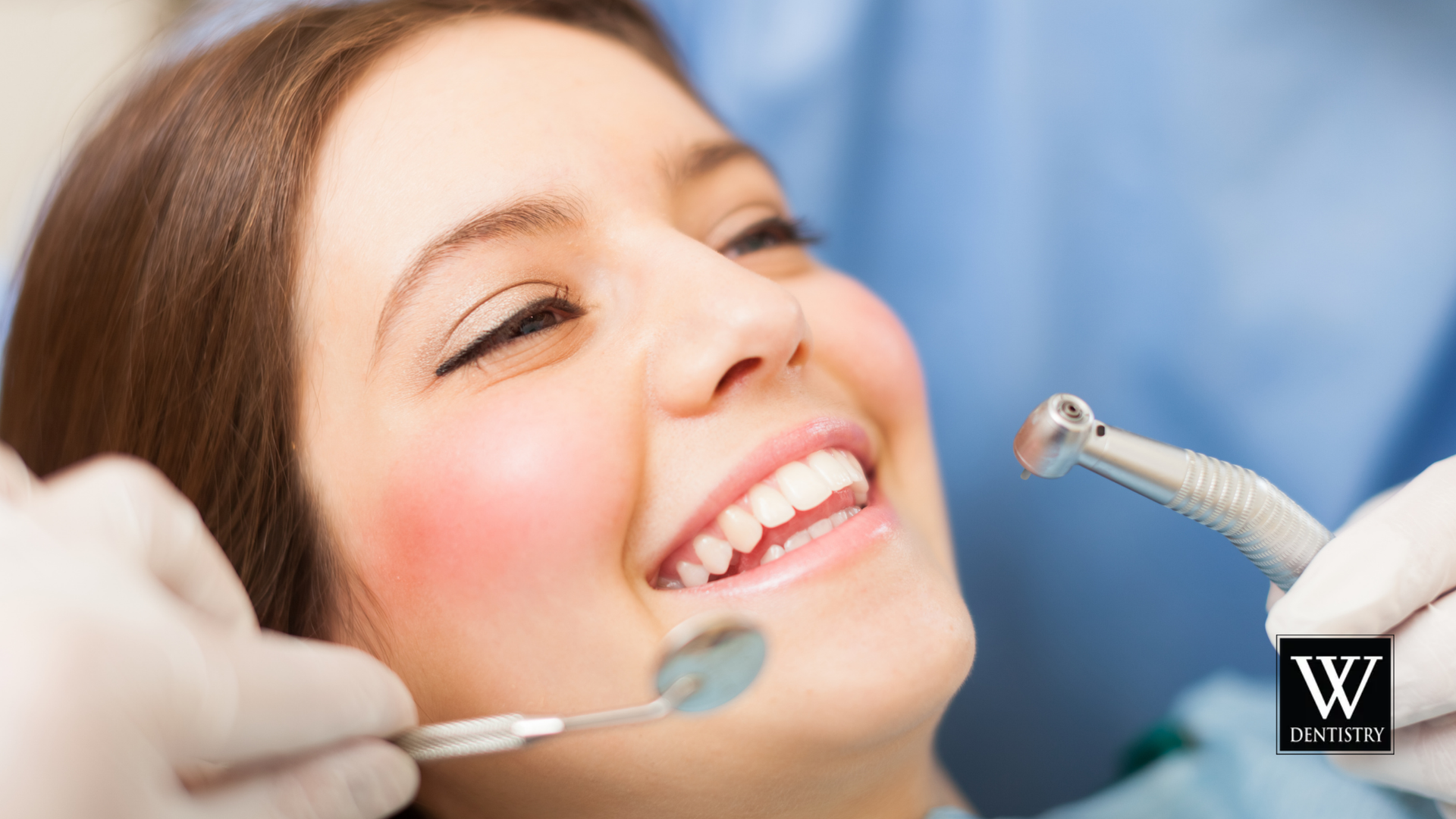 Woman in dental chair, smiling; dentist using tools to examine teeth.