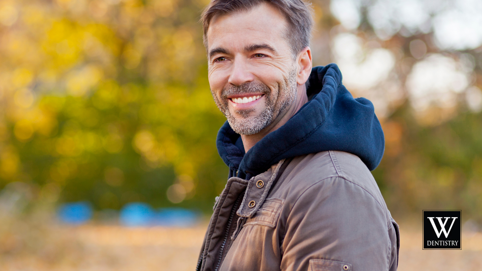A man wearing a hoodie and a jacket is smiling.