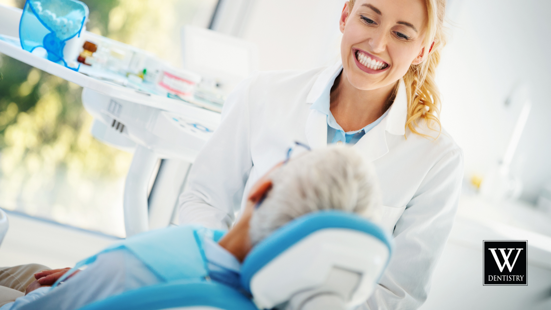 A dentist is smiling while talking to a patient in a dental chair.