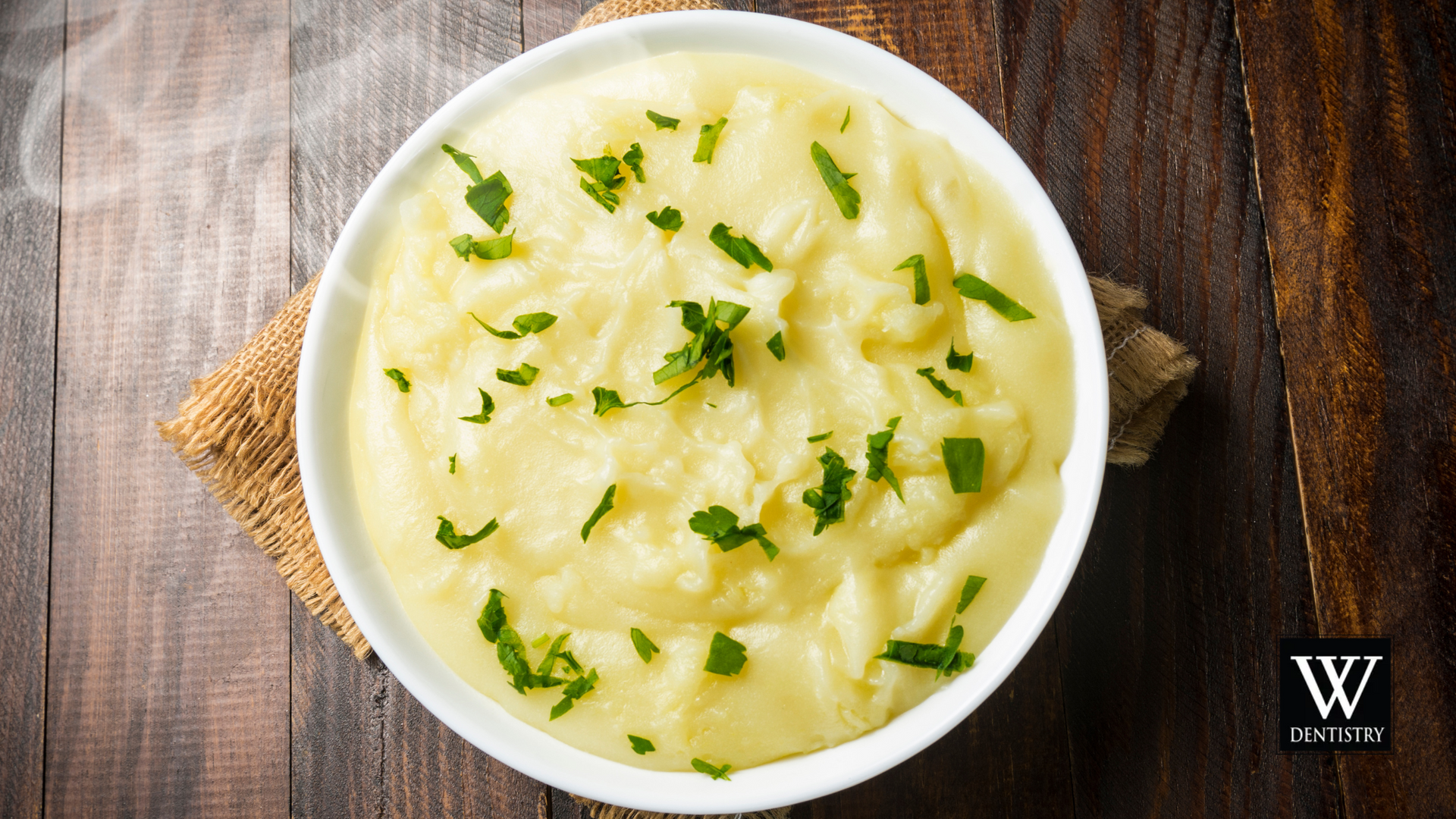 A bowl of mashed potatoes with parsley on a wooden table.