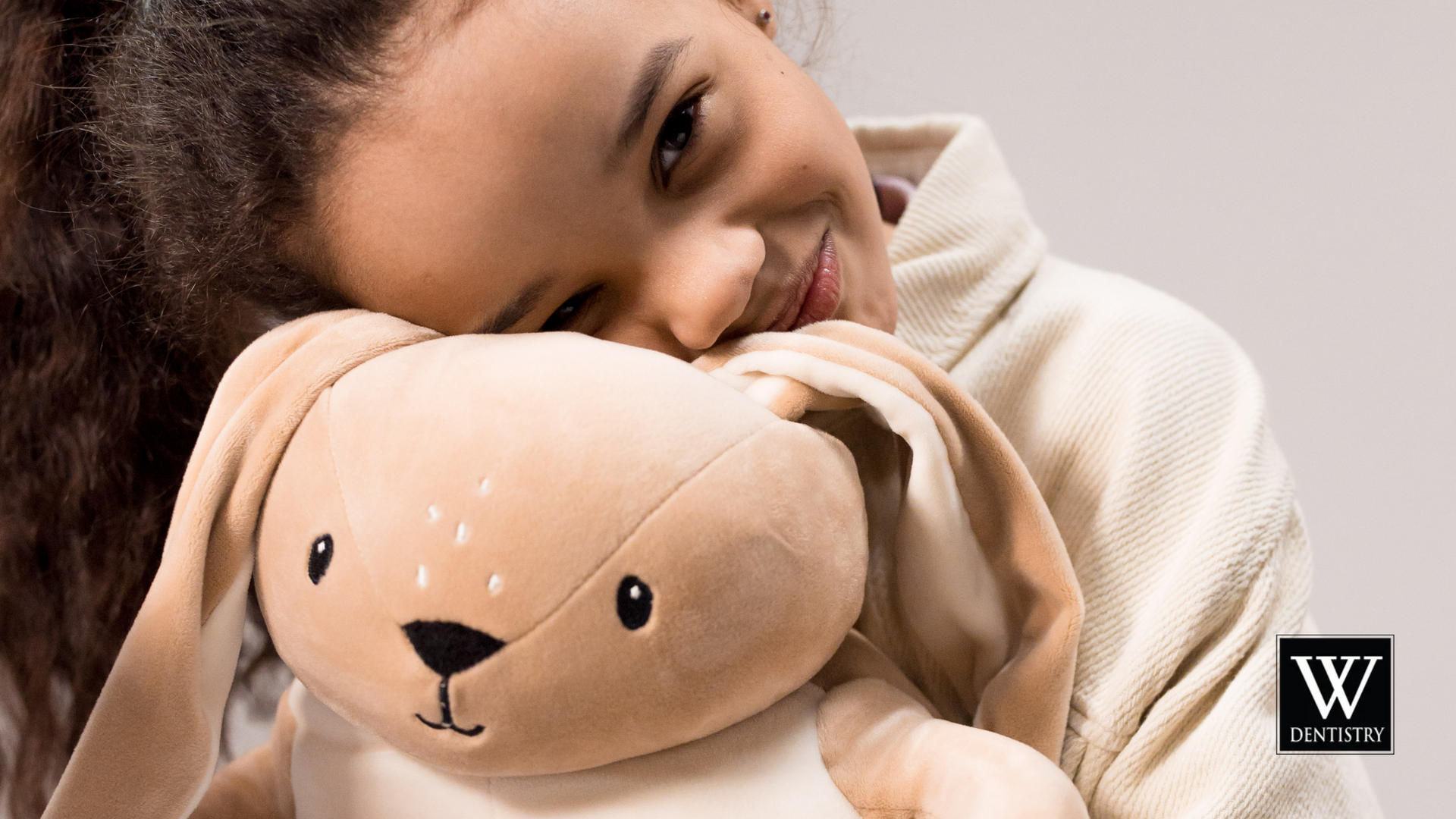 A little girl is holding a stuffed animal with the letter w on it