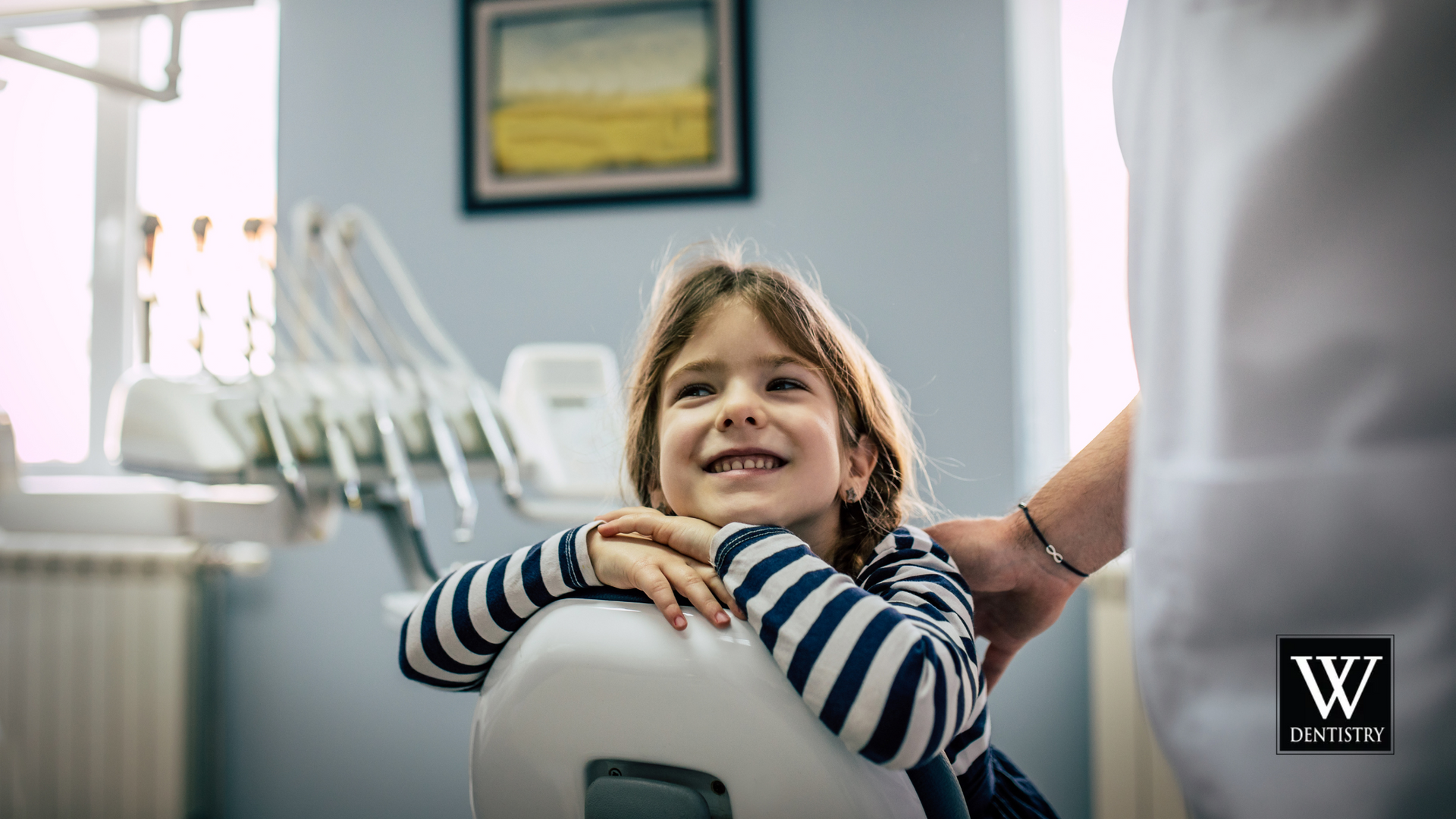A little girl is sitting in a dental chair and smiling at the dentist.