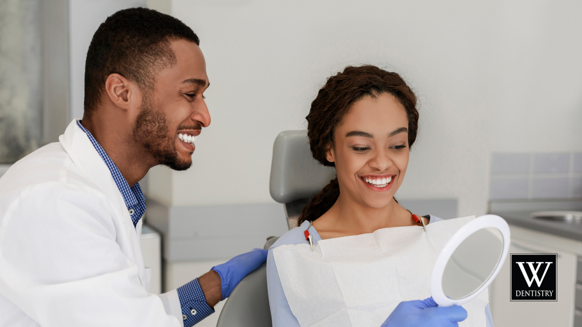 A dentist is talking to a woman in a dental chair while she looks at her teeth in a mirror.