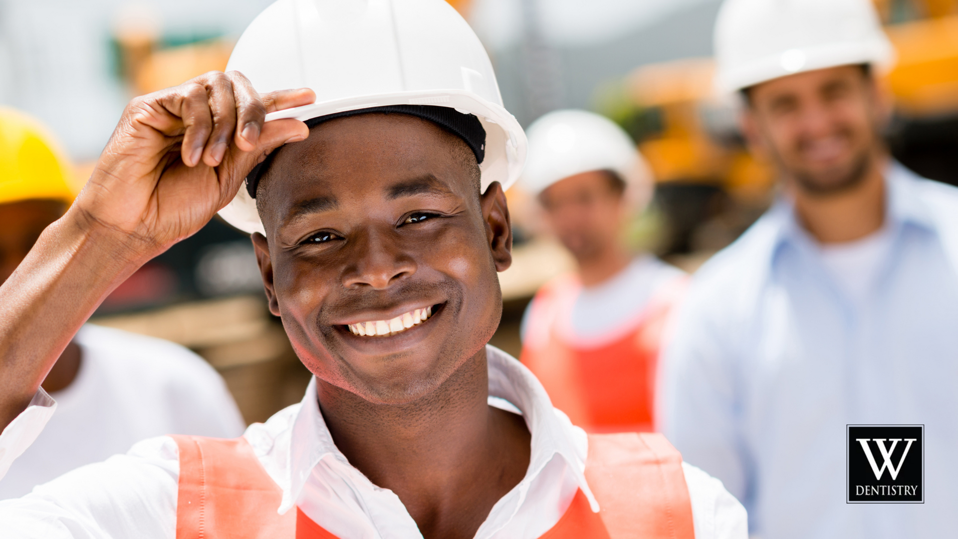 A man wearing a hard hat is smiling while standing in front of a group of construction workers.