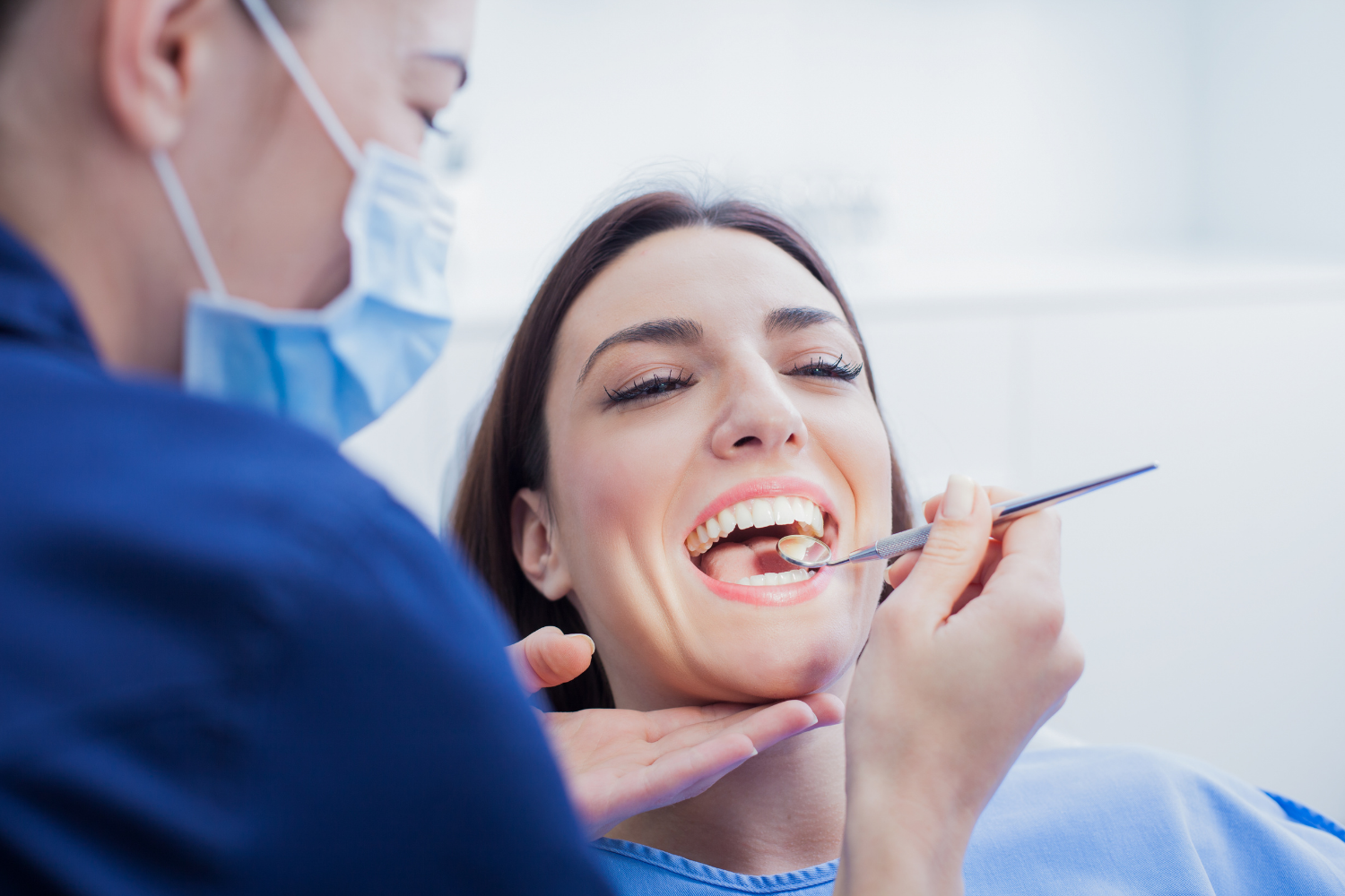 Dentist examining a smiling patient’s teeth with a dental mirror and tools