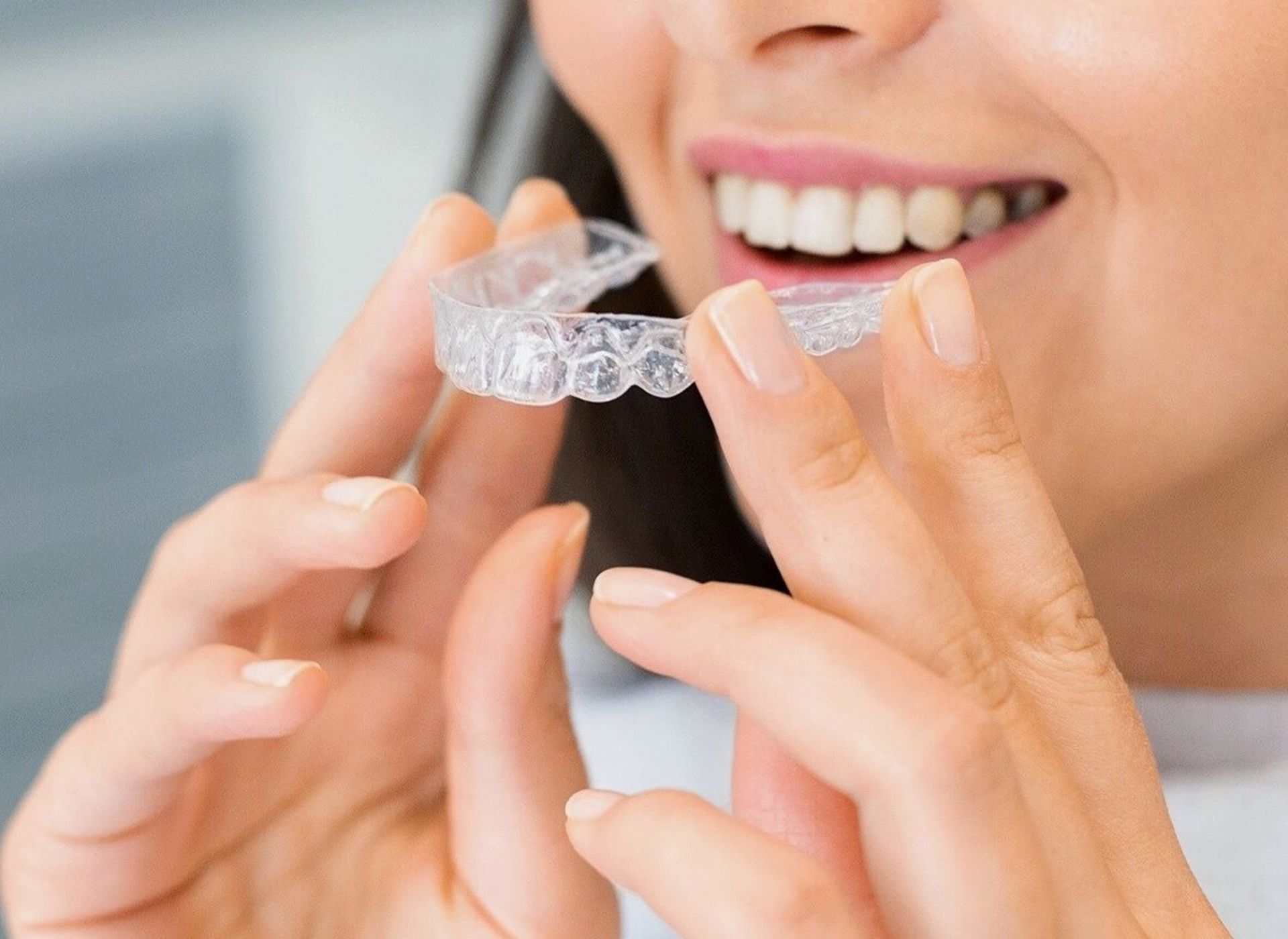 Person smiling while holding a clear dental aligner near their teeth