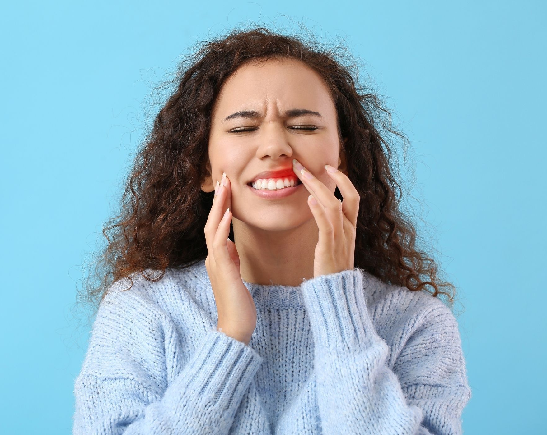 Woman grimacing and pressing her cheeks, showing tooth pain against a blue background