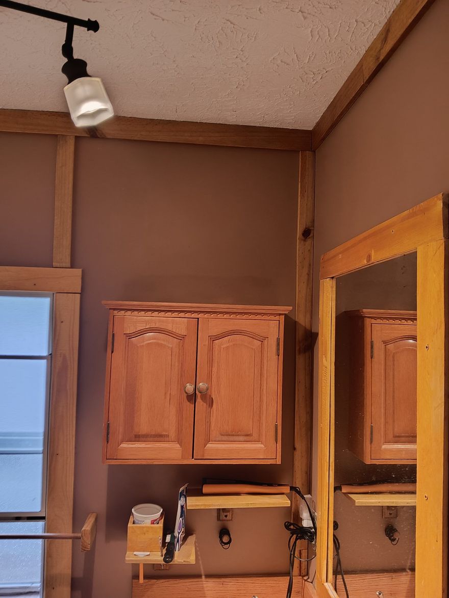 Brown kitchen wall with wooden cabinets, a window, and a ceiling track light, seen beside a doorway mirror