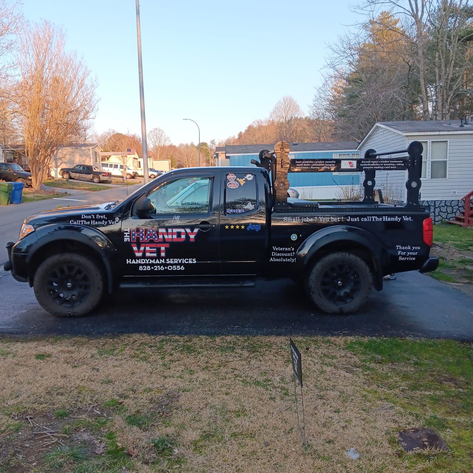 Black utility pickup truck parked in a suburban driveway beside a house at dusk