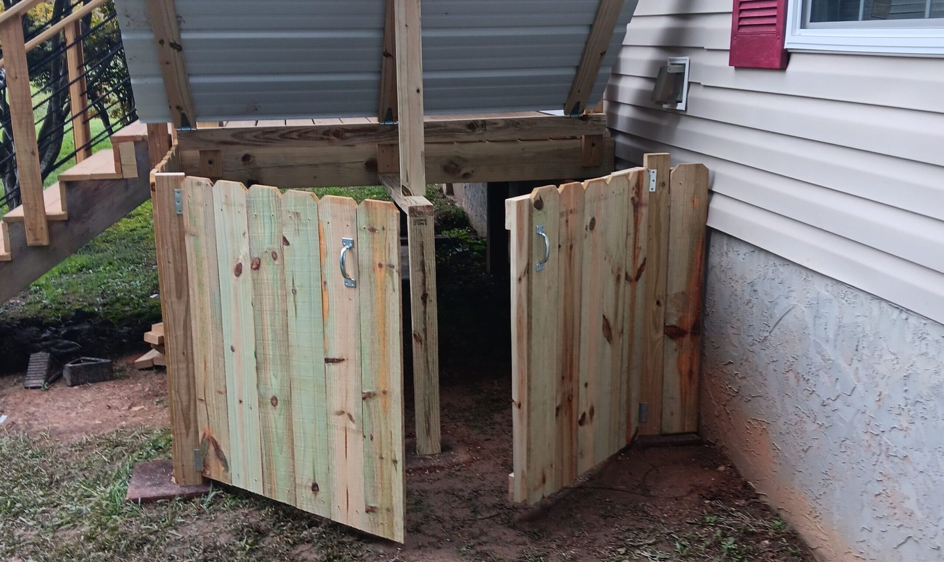 Wooden garden shed gate with weathered panels beside a house under a covered porch