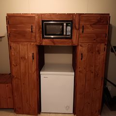 Wooden kitchen cabinet with built-in microwave above a white mini fridge on a beige wall.