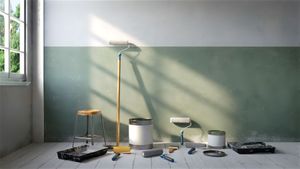Paint supplies and tools arranged in a sunlit room with pale green walls and a window.