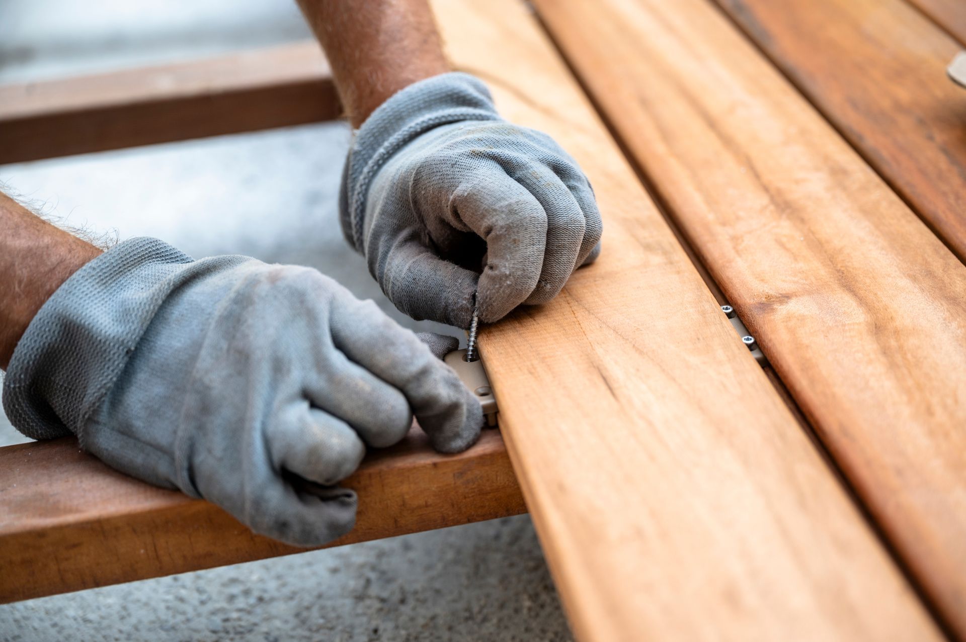 Gray work gloves assembling a wooden bench plank outdoors