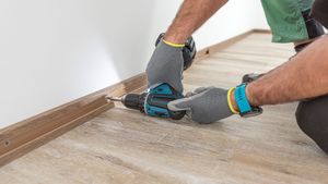 Hands using a power drill to install trim along a wooden floor edge