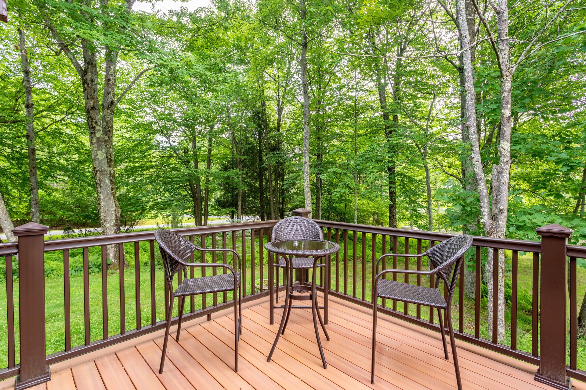Wooden deck with bistro table and chairs overlooking a lush green wooded yard