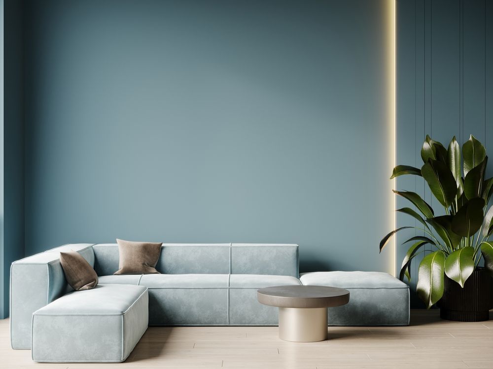 A light blue sectional sofa sits against a matching wall with integrated vertical lighting next to a large potted plant.