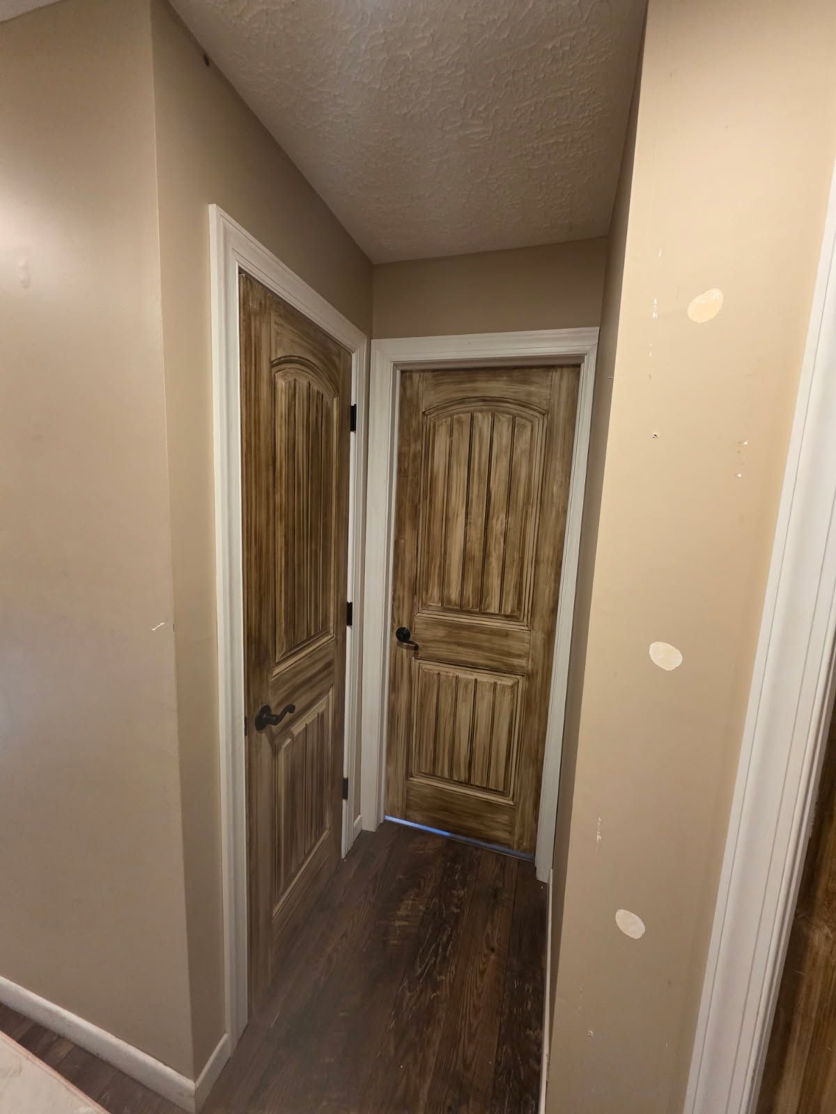 A hallway with light tan walls, dark wood-textured doors, and dark wood flooring.