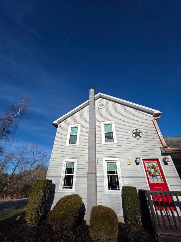 A two-story light gray house with a vertical chimney, a red front door, and a decorative star under a bright blue sky.