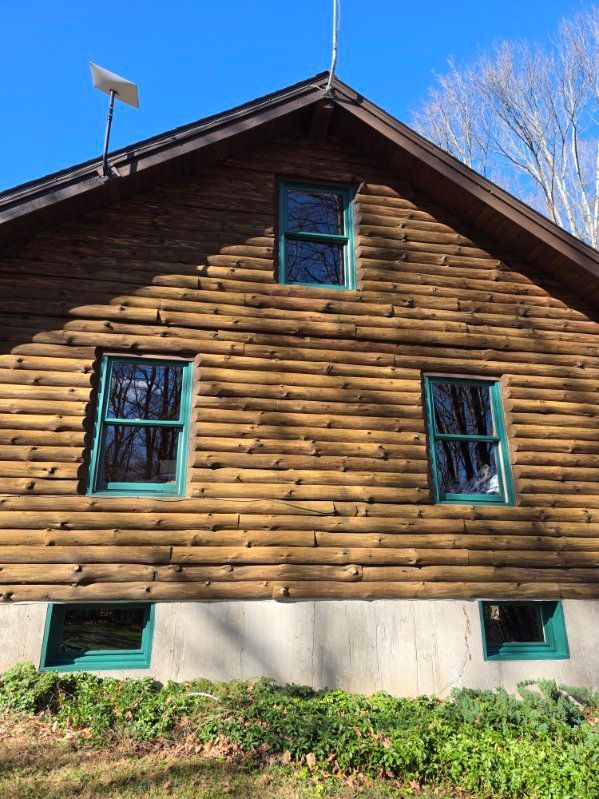 Log cabin exterior with green-framed windows, a concrete foundation, and a satellite dish on the roof.