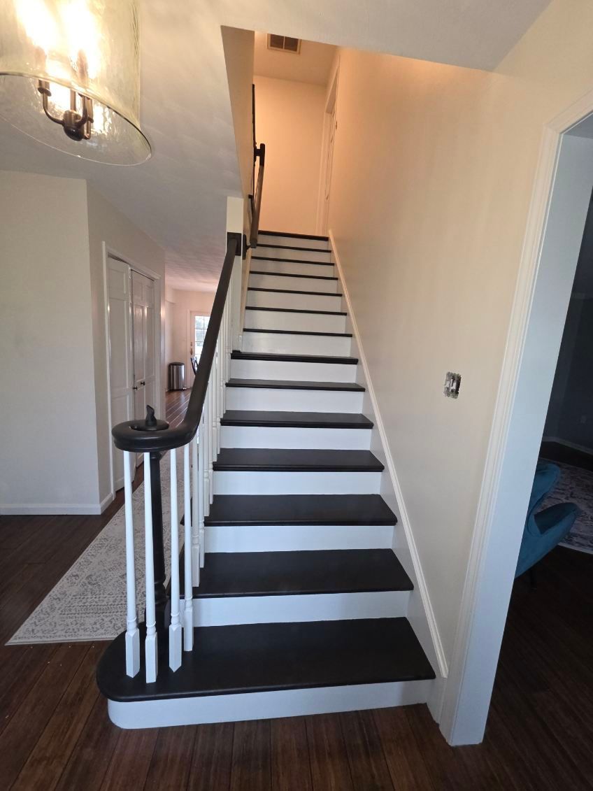 A straight staircase with black treads and white risers, featuring a white railing with a dark handrail in a bright home.