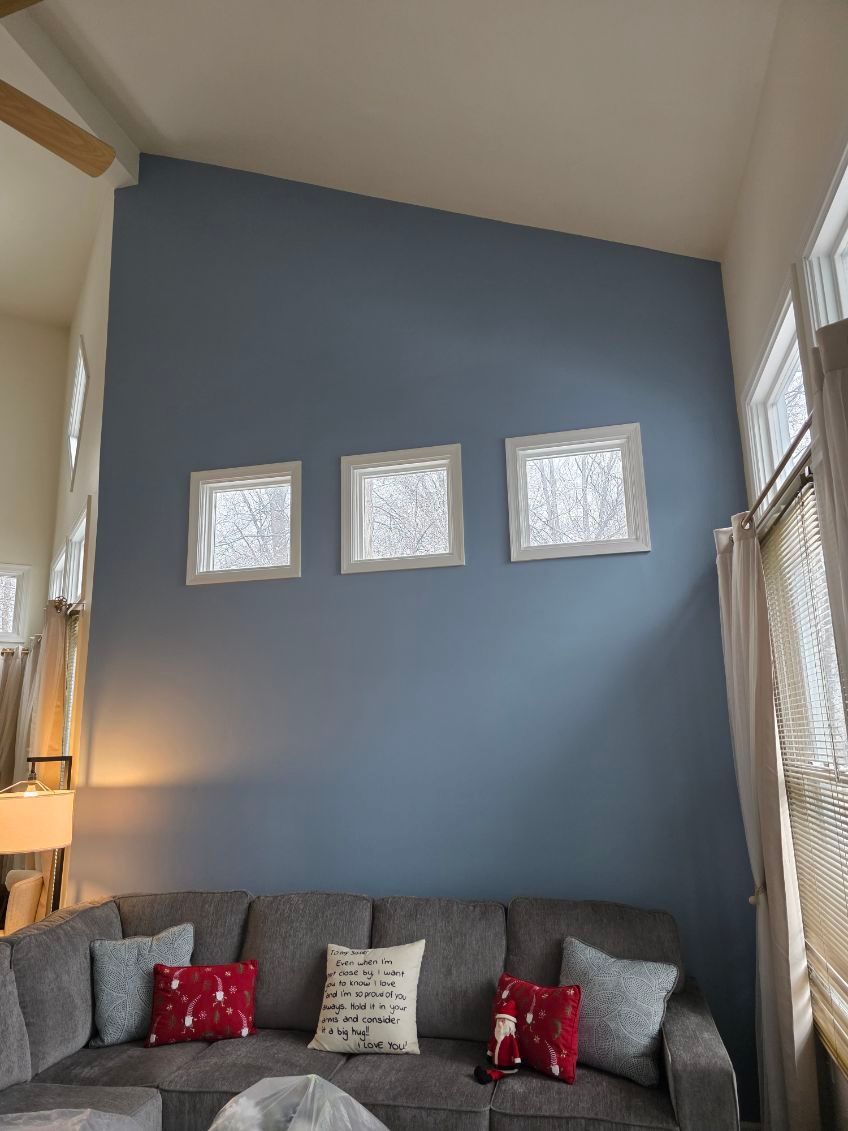 A grey sofa sits against a tall, slate-blue wall with three small, evenly spaced square windows.