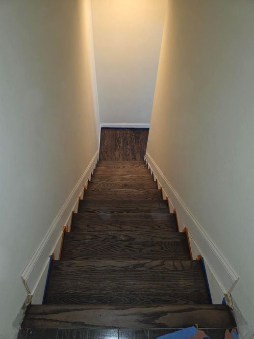 A downward view of a residential staircase with dark wood treads and white walls.