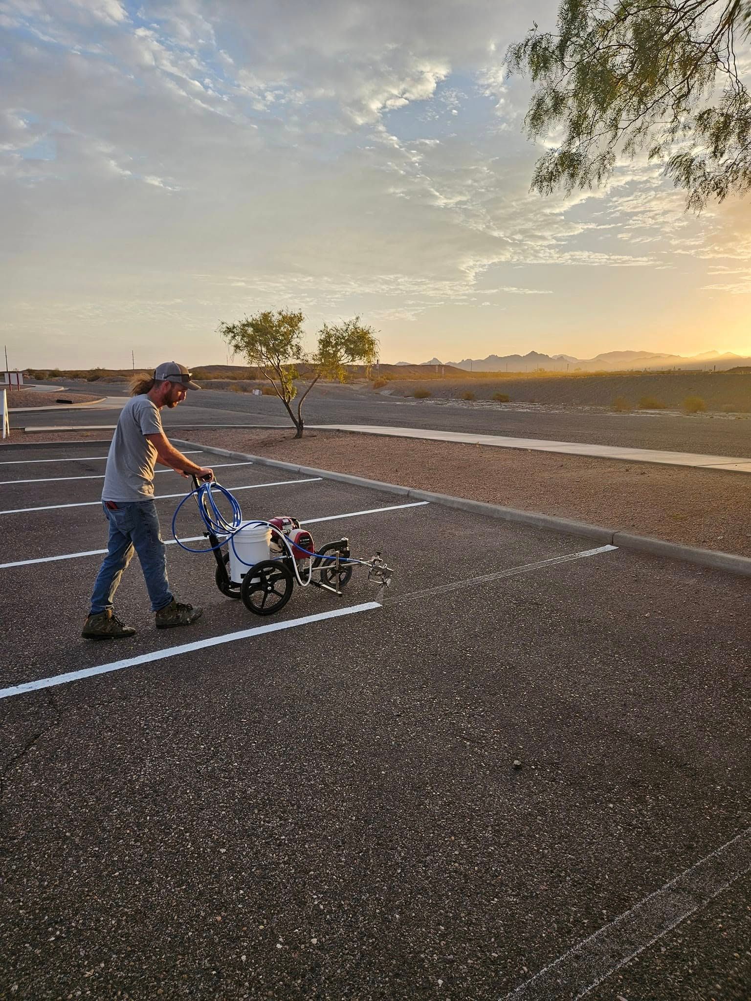 Person pushing a stroller on an empty paved area at sunset with mountains in the distance