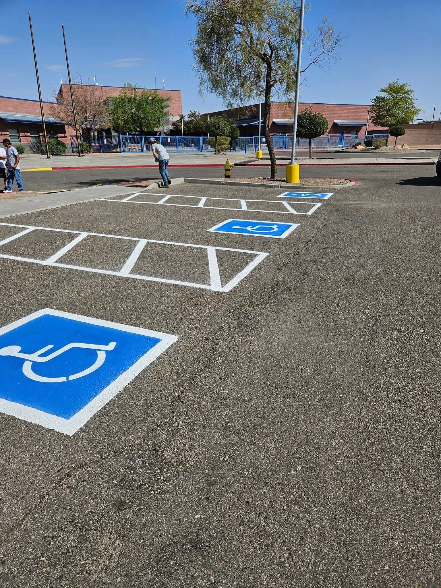 Accessible parking spaces marked on asphalt in a school parking lot, with children in the background.