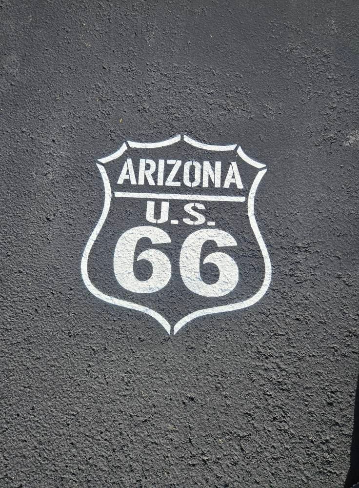 White Arizona U.S. Route 66 shield logo on a dark textured pavement background