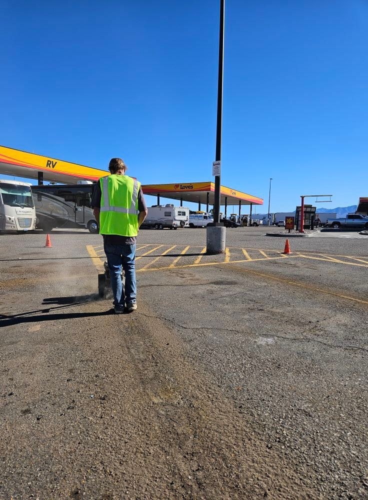Worker in a neon safety vest walking on a road near a gas station under a clear blue sky