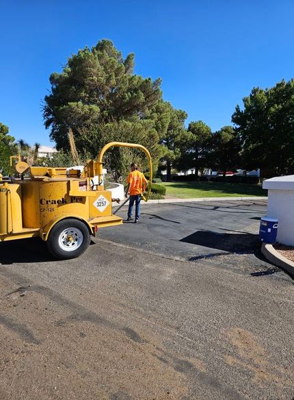 Worker in orange vest beside yellow wood chipper on a paved lot under a blue sky