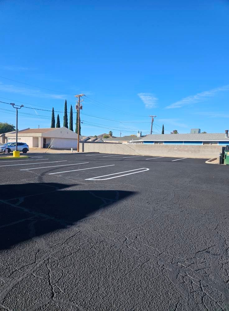 Empty paved lot with painted parking lines under a clear blue sky, buildings and utility poles in the background