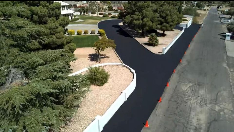 Fresh black asphalt laid along a curved residential road beside landscaped yards and trees.