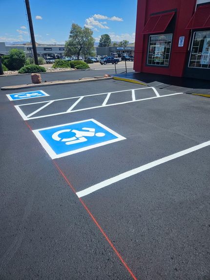 Accessible parking spaces and striped loading zone beside a red building on a sunny day