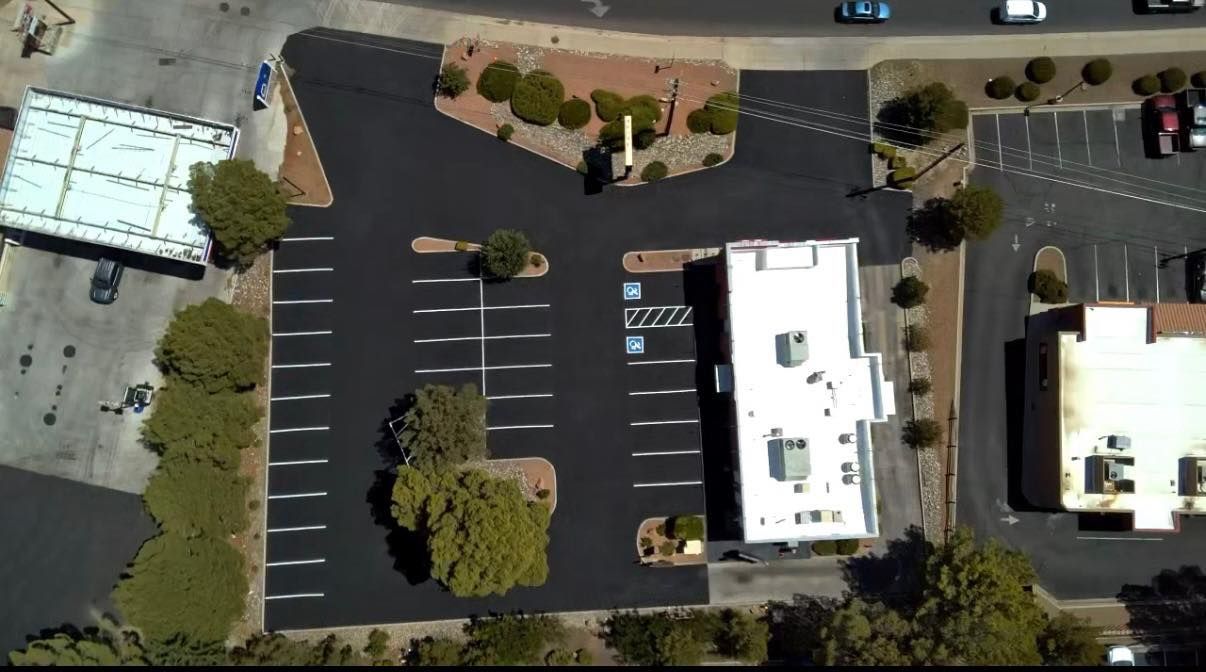 Aerial view of a parking lot beside two white buildings with trees and landscaped areas.