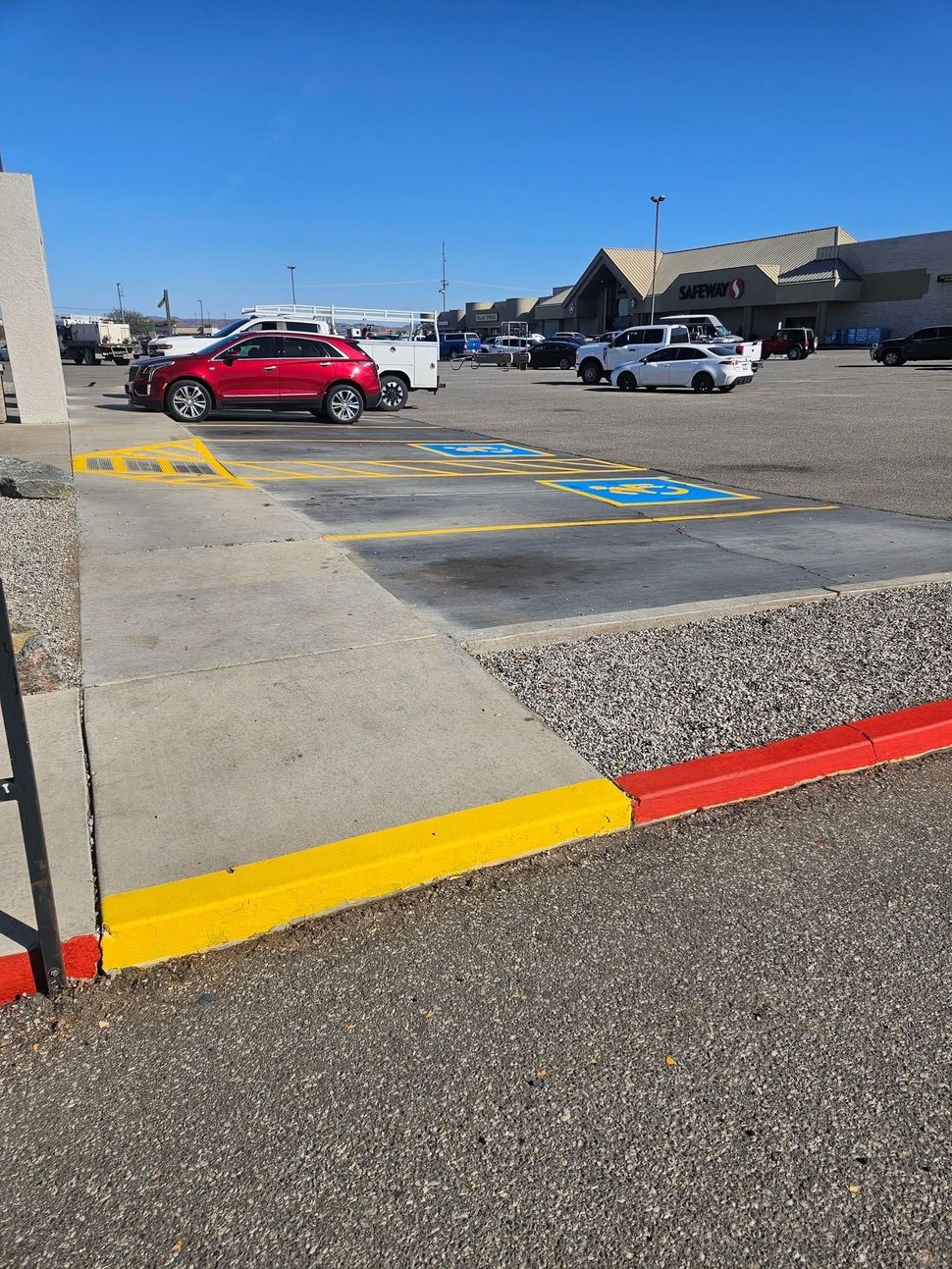 Accessible parking spaces and curb ramp in a parking lot, with cars and a shopping center in the background.