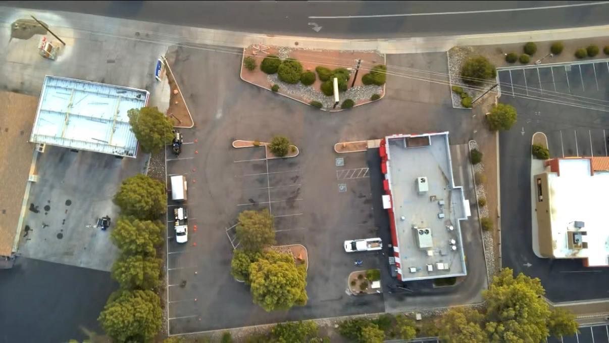 Aerial view of a parking lot with several cars, trees, and adjacent buildings near a curved road.