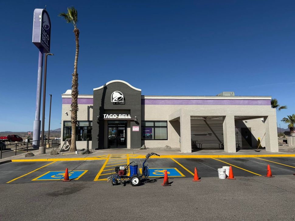 Taco Bell restaurant exterior with purple trim, parking lot, and clear blue sky