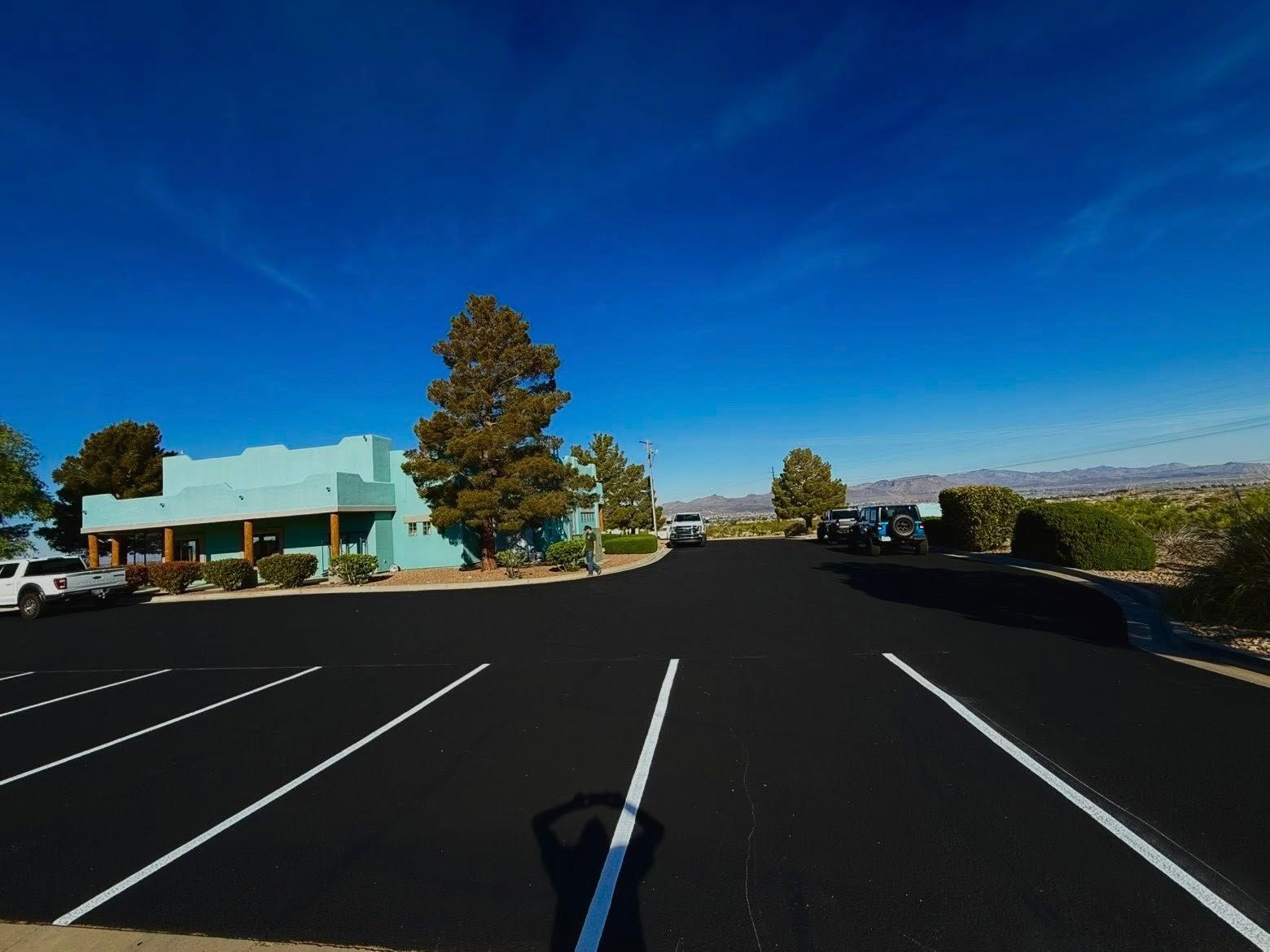 Empty parking lot beside a low building under a bright blue sky.
