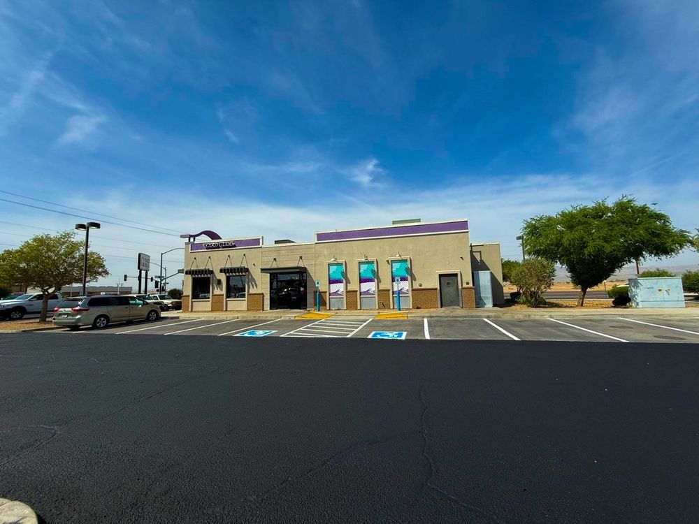 Low beige storefront in a parking lot under a bright blue sky with a few trees and parked cars