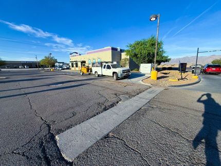 Yellow utility truck parked beside a yellow building in a cracked asphalt lot under a blue sky.