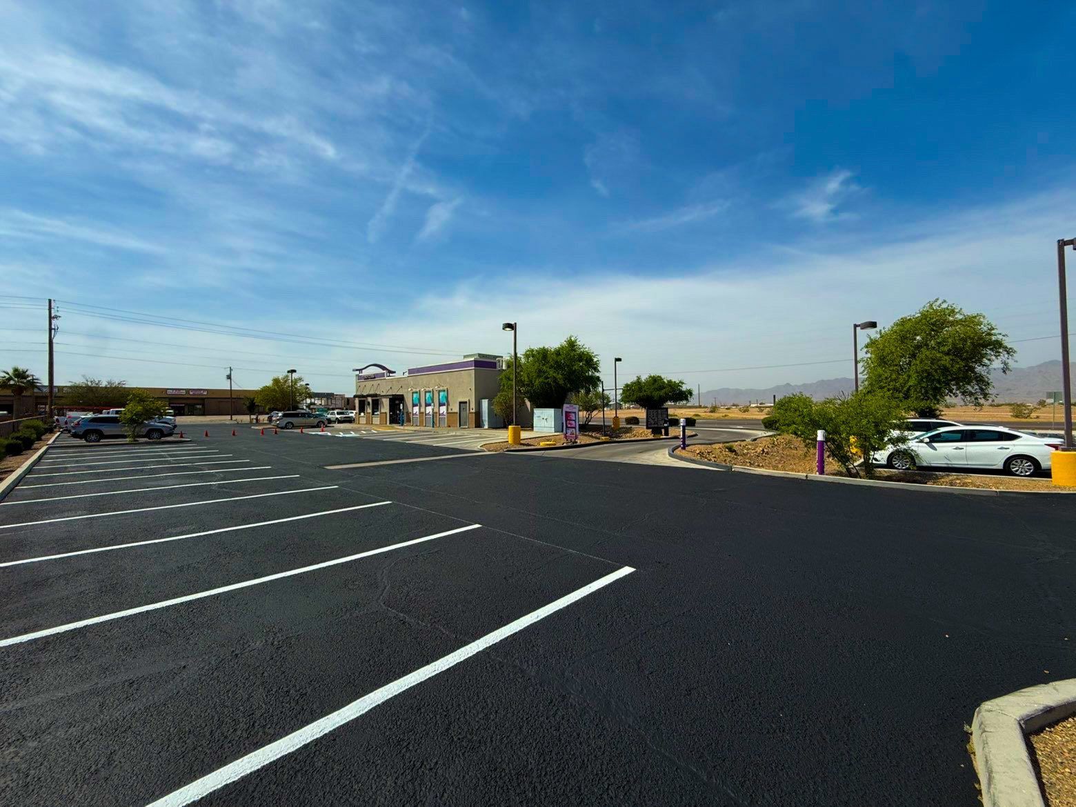 Empty parking lot with white-striped spaces, a low building, and trees under a clear blue sky