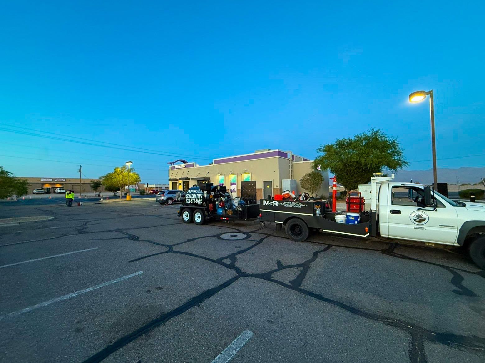 Tow truck with equipment parked in a lot beside a beige building at dusk