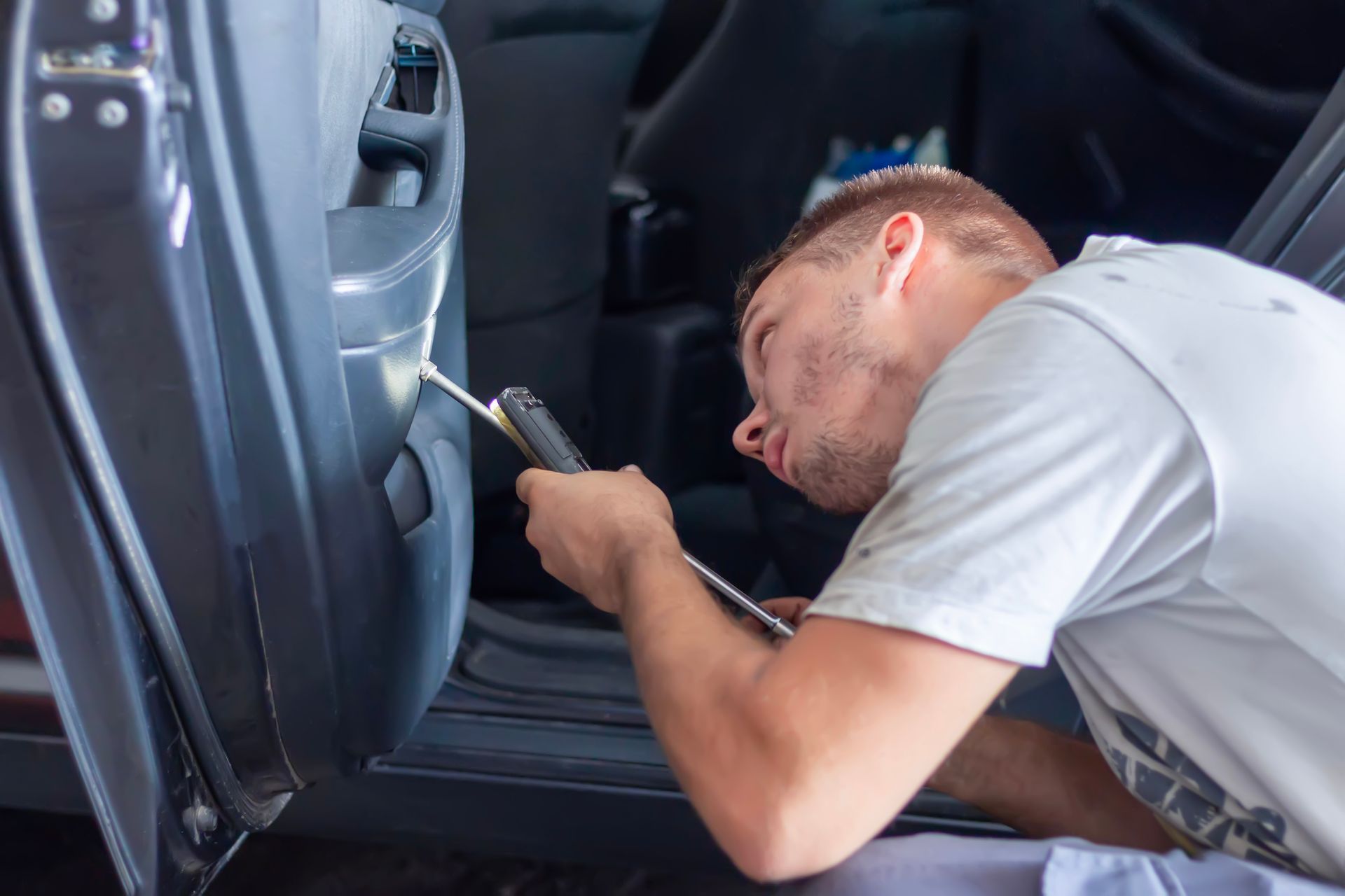 A technician uses a screwdriver to repair a car door's lock mechanism from inside.