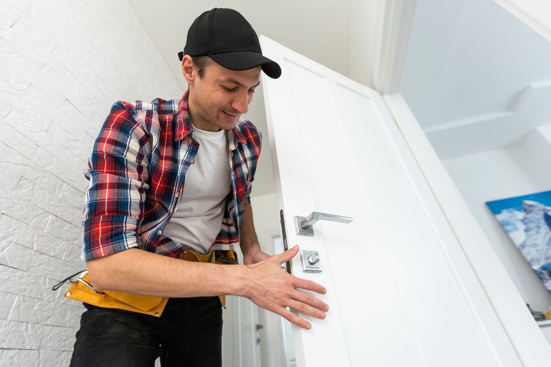 A locksmith wearing a hat and plaid shirt is in the process of checking a door lock.